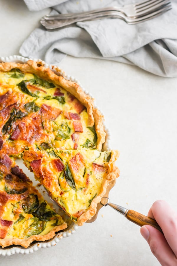 A hand lifting a slice of quiche out of the pan.