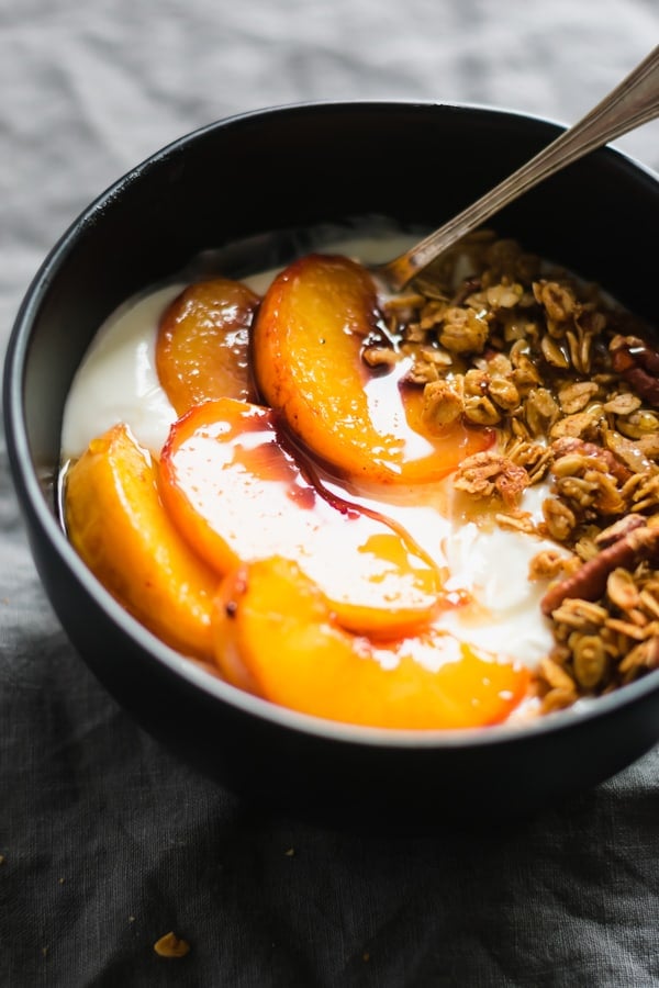 A bowl of greek yogurt with roasted peaches and maple granola. 