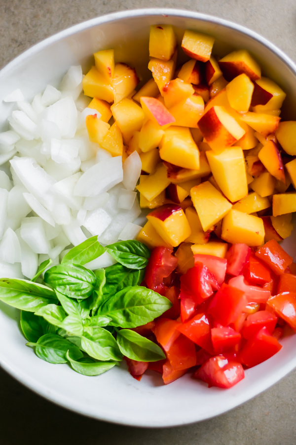 Chopped peaches, onions, tomatoes, and basil in a bowl.