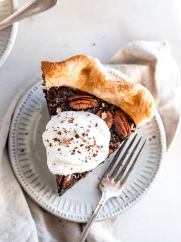 Piece of chocolate bourbon pie topped with whipped cream on a white plate.