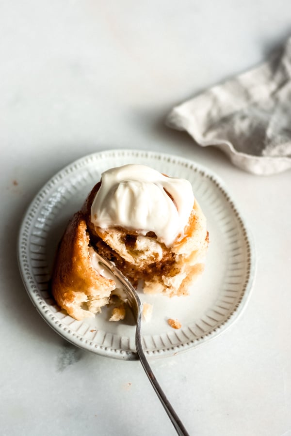 A maple brioche cinnamon roll with cream cheese frosting on a plate.