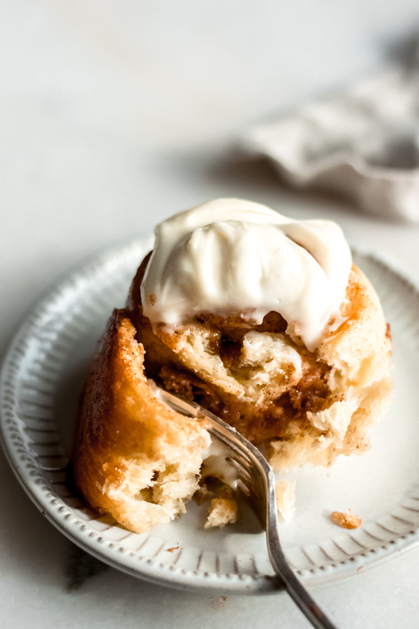 A maple brioche cinnamon roll with cream cheese frosting on a plate.
