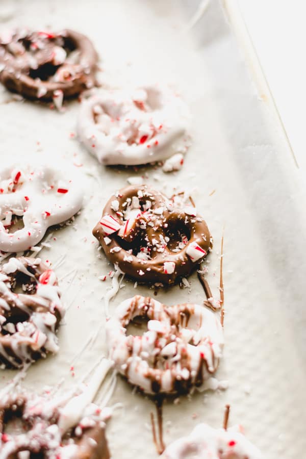 Chocolate dipped pretzels covered in crushed peppermint on a wax paper lined baking sheet.