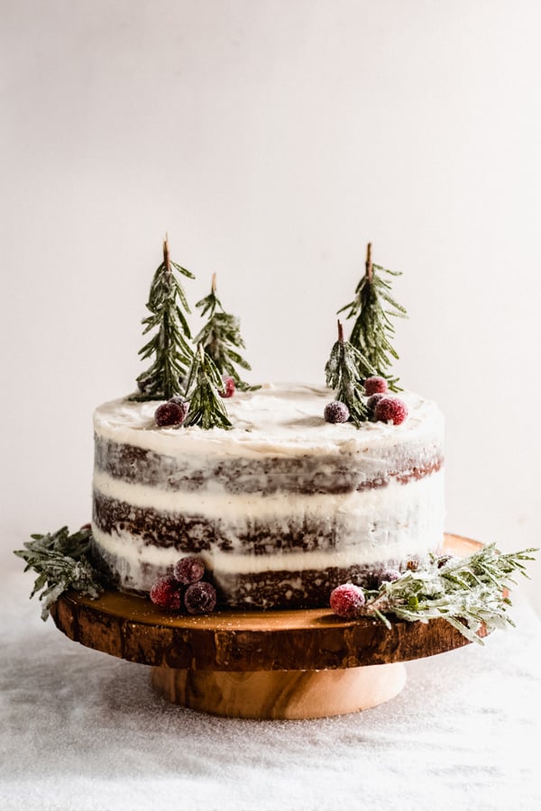 A naked frosted gingerbread cake on a wooden cake stand.