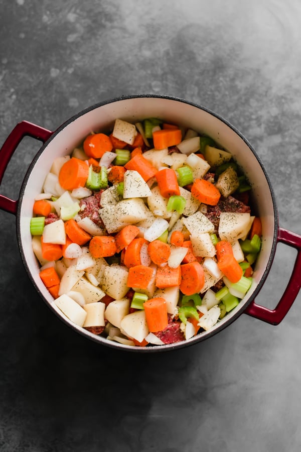A dutch oven filled with the lamb stew meat, potatoes, carrots, onion, celery, and seasoning.