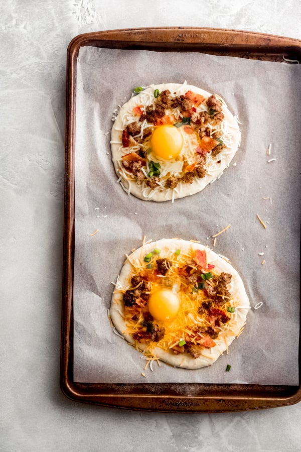 Breakfast pizzas assembled on a baking tray.