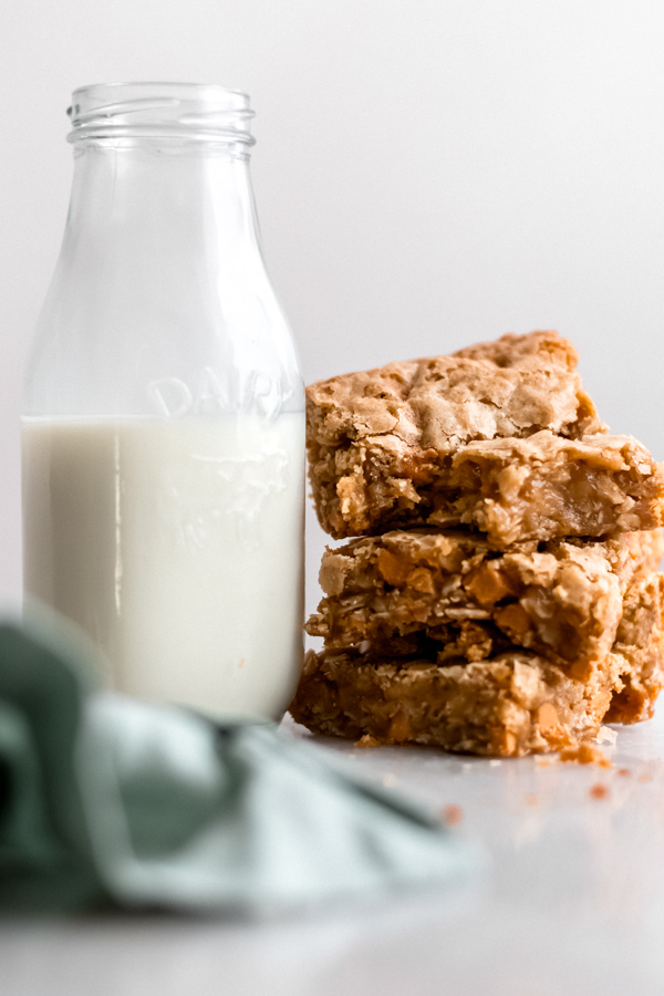 A stack of butterscotch blondies and a glass bottle of milk.