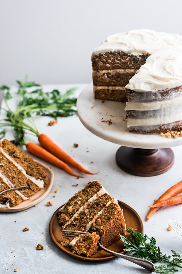 Carrot cake slices on plates and whole cake on a cake stand.