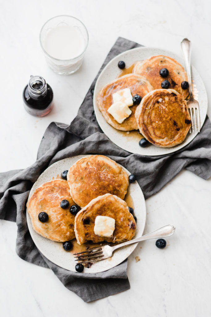 Blueberry pancakes with butter and syrup on plates.