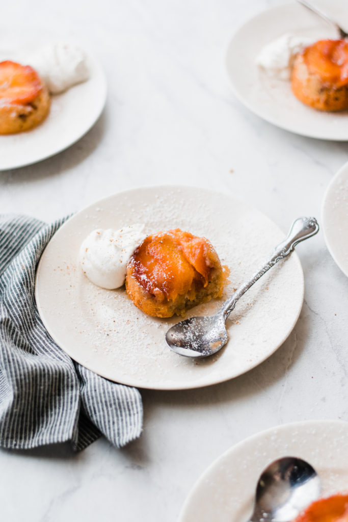 Mini peach upside down cakes with nutmeg spiced whipped cream on plates.