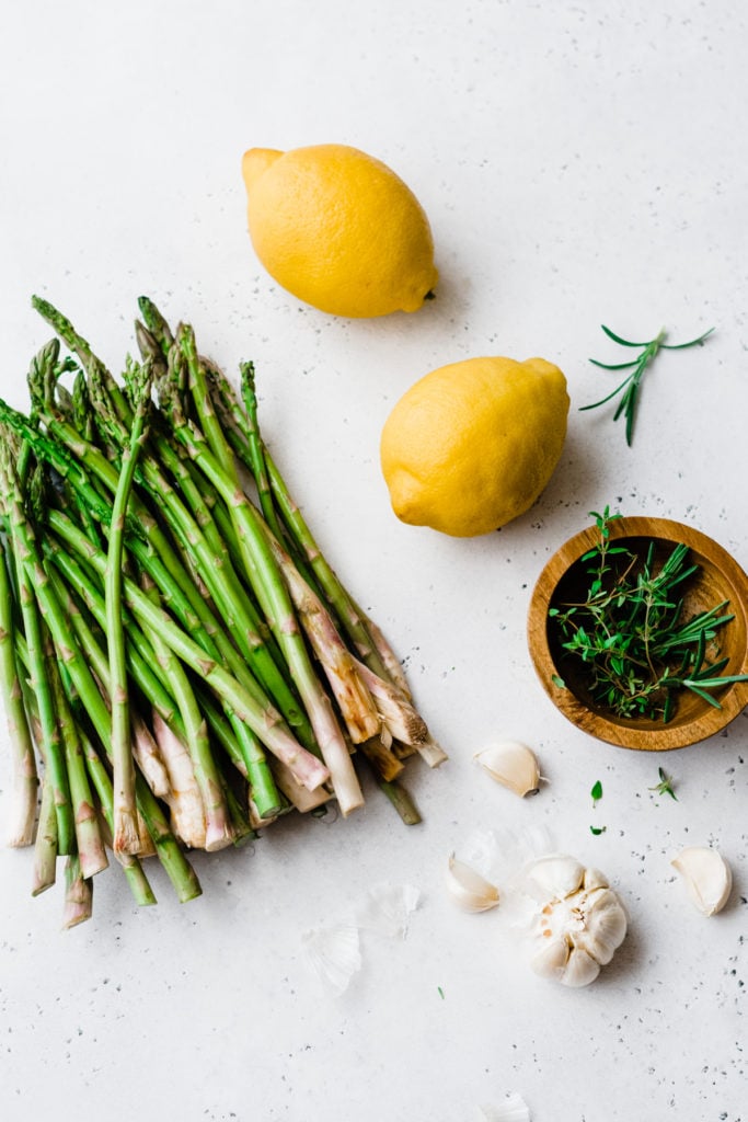 Asparagus, garlic, and lemons on a white surface.