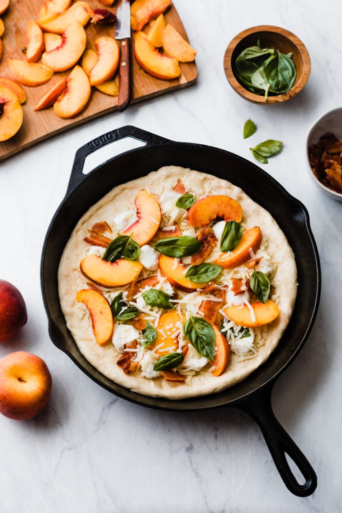 Peach pizza assembled on dough in a cast iron skillet.