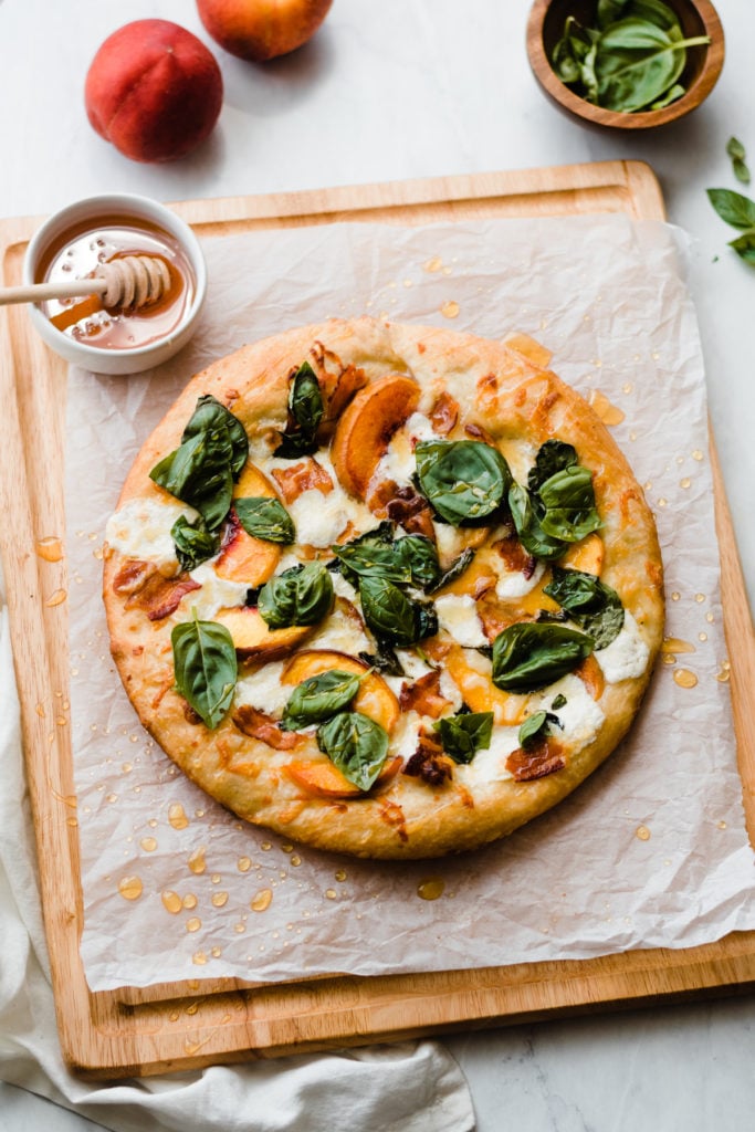 Peach pizza on a wooden cutting board.