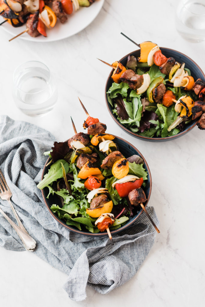 Grilled lamb kebabs on top of a  salad in a bowl.