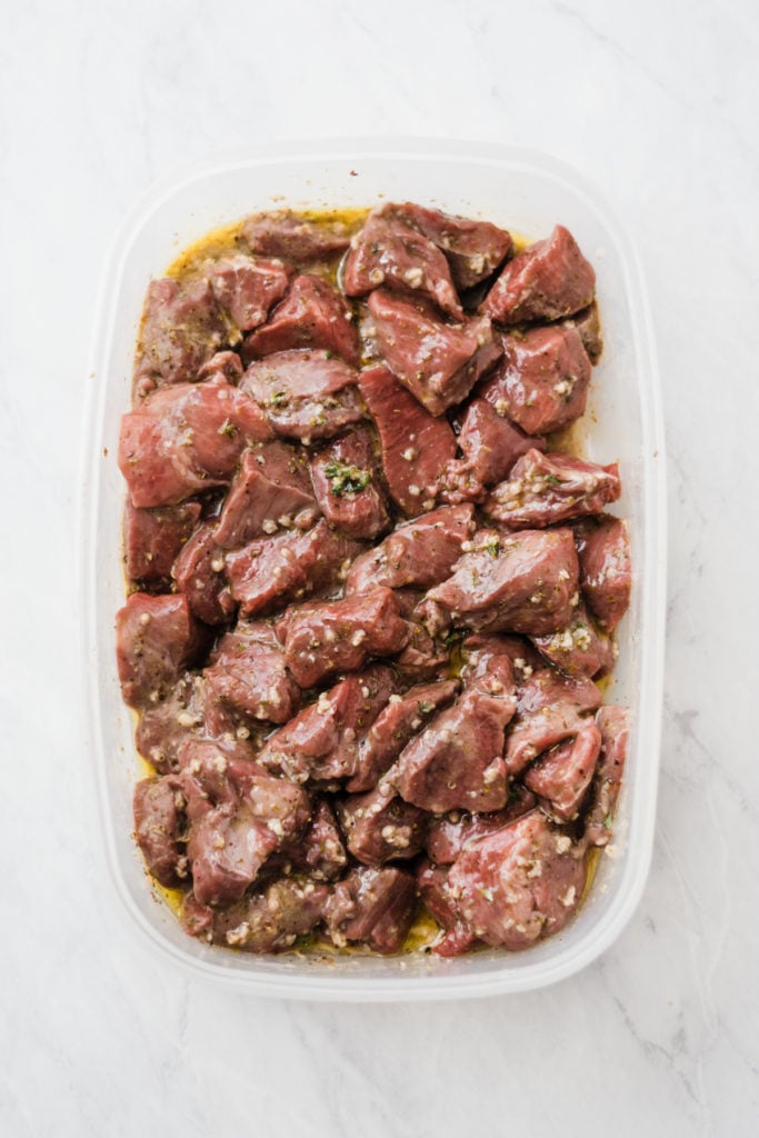 Raw lamb chunks marinating in a container.