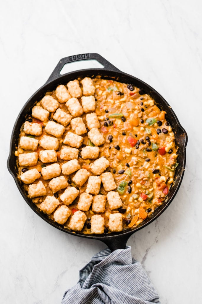 Tater tots placed on one half of the skillet over the filling.