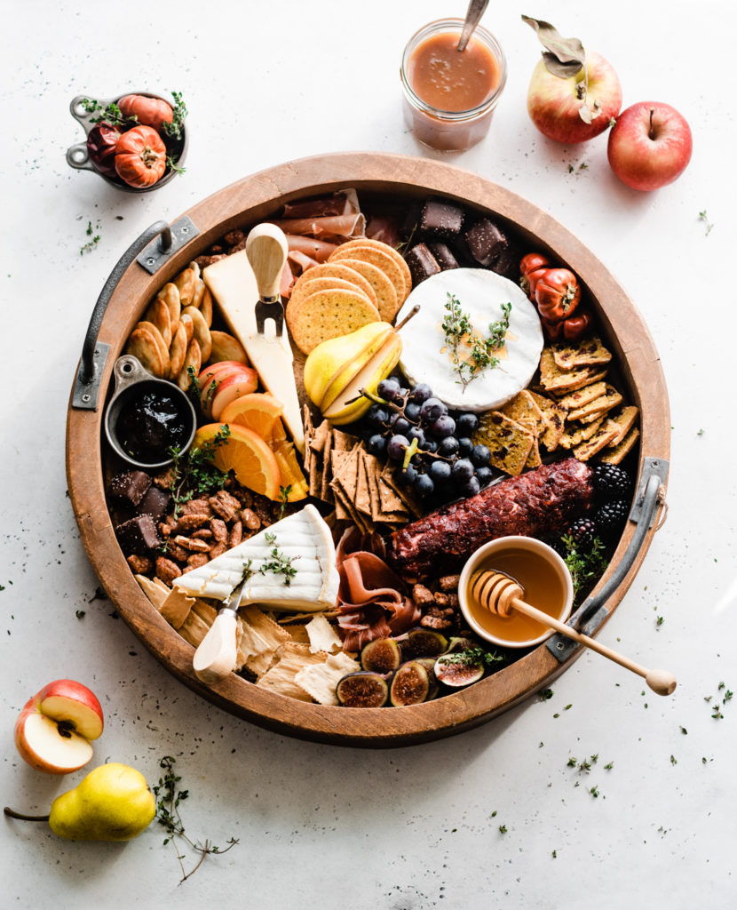 A fall harvest cheeseboard filled with crackers, cheese, meats, fruit, and nuts.