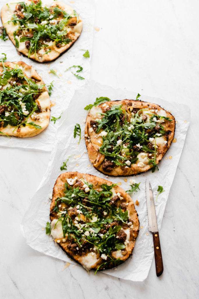 Grilled Lamb Pizzas with Arugula + Honey - Grilled Lamb Pizzas are crazy delicious, but simple enough to make for a game-day watch party or tailgate – everything can be prepped ahead! Made with naan bread, caramelized onions, feta + mozzarella cheese, ground lamb, fresh arugula, and a drizzle of honey. #lamb #pizza #pizzarecipes #tailgating #grilling #grillingrecipes #mozzarella #easyrecipe #dinnerrecipes #gameday #gamedayfood #gamedayrecipes #comfortfood| bluebowlrecipes.com