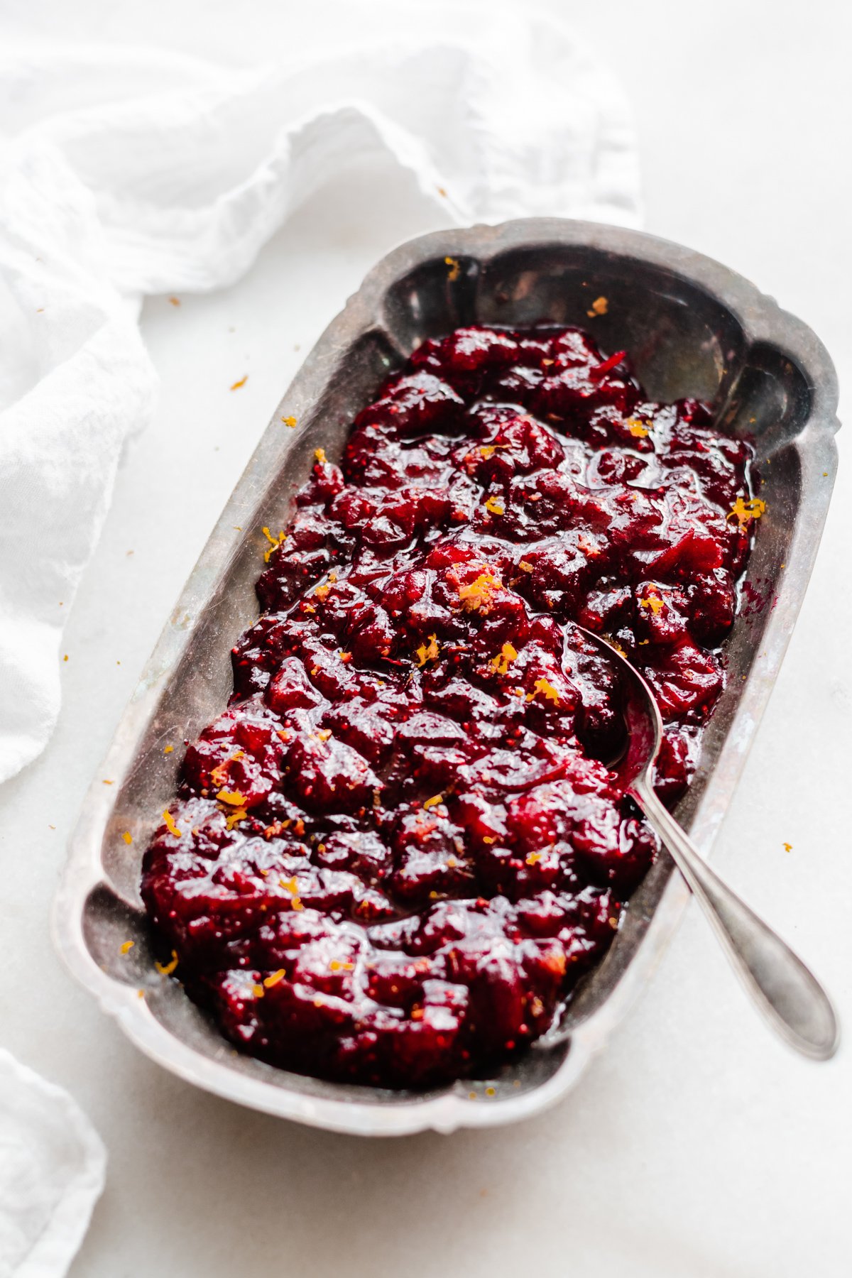 A serving dish of cranberry sauce with a spoon digging in.