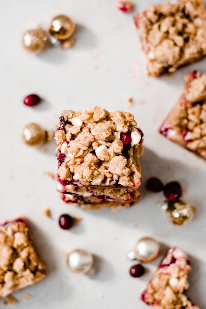 Cranberry White Chocolate Crumble Bars - These bars come together so quickly - there's no mixer required & the crumble dough doubles as the base and topping for this festive treat! Use homemade or store bought cranberry sauce for the filling, and pile on the white chocolate chips. This is a dessert you won't be able to put down! #cranberry #chocolate #christmascookies #christmasrecipes #christmasbaking #dessertrecipes #dessertbars #holidaybaking #christmasbaking | bluebowlrecipes.com
