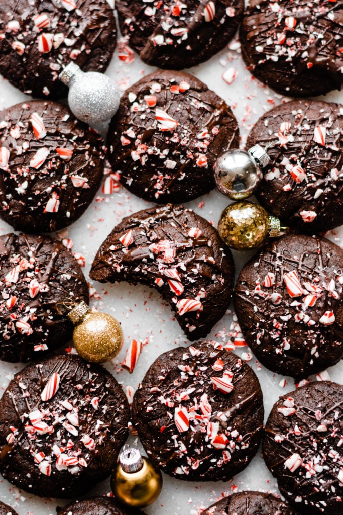 Peppermint mocha cookies drizzled with chocolate and sprinkled with crushed candy canes on a marble surface.
