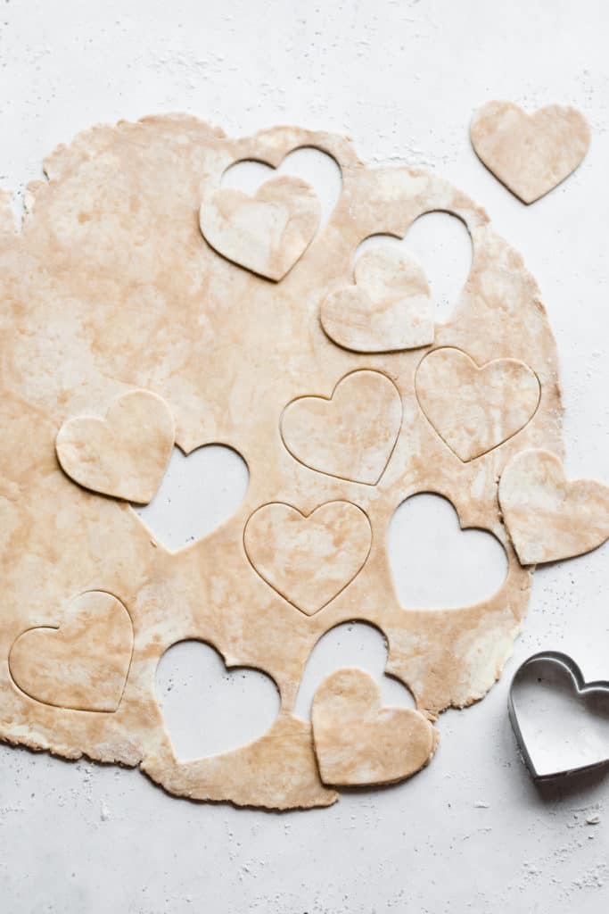 Rolled out pie dough with heart shapes cut out.