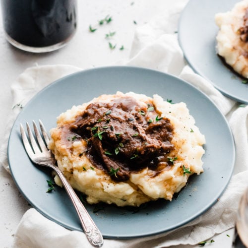 Short ribs on a bed of cheddar mashed potatoes, on plates.