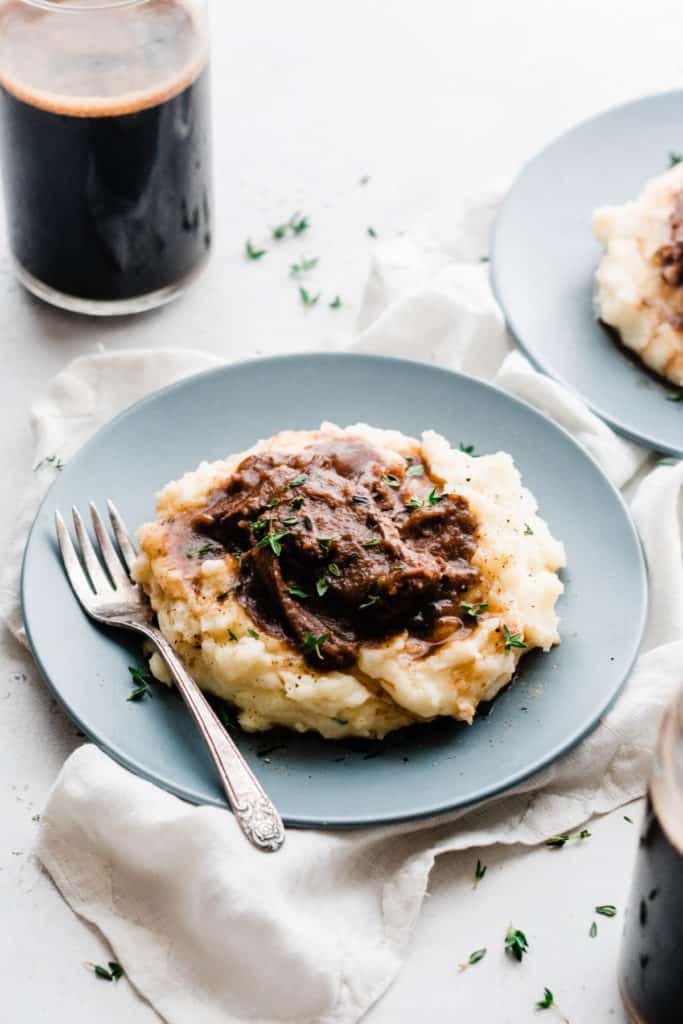 Short ribs on top of mashed potatoes on a plate.