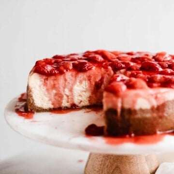 Sliced cheesecake on a cake stand with strawberry topping.