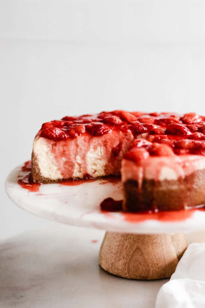 The sliced cheesecake on a cake stand with the strawberry topping on top. 