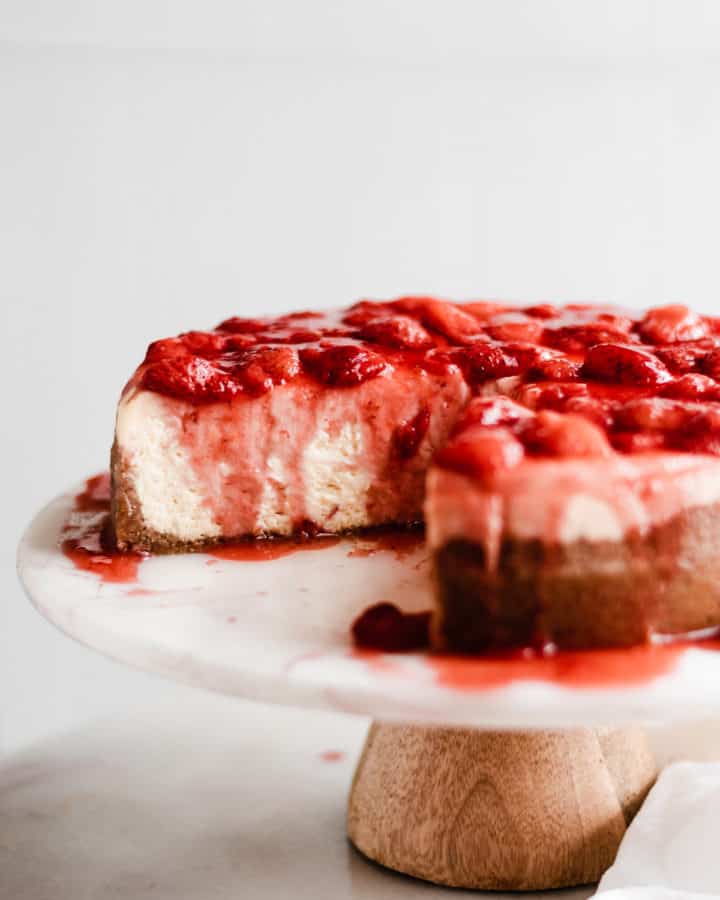 Sliced cheesecake on a cake stand with strawberry topping.