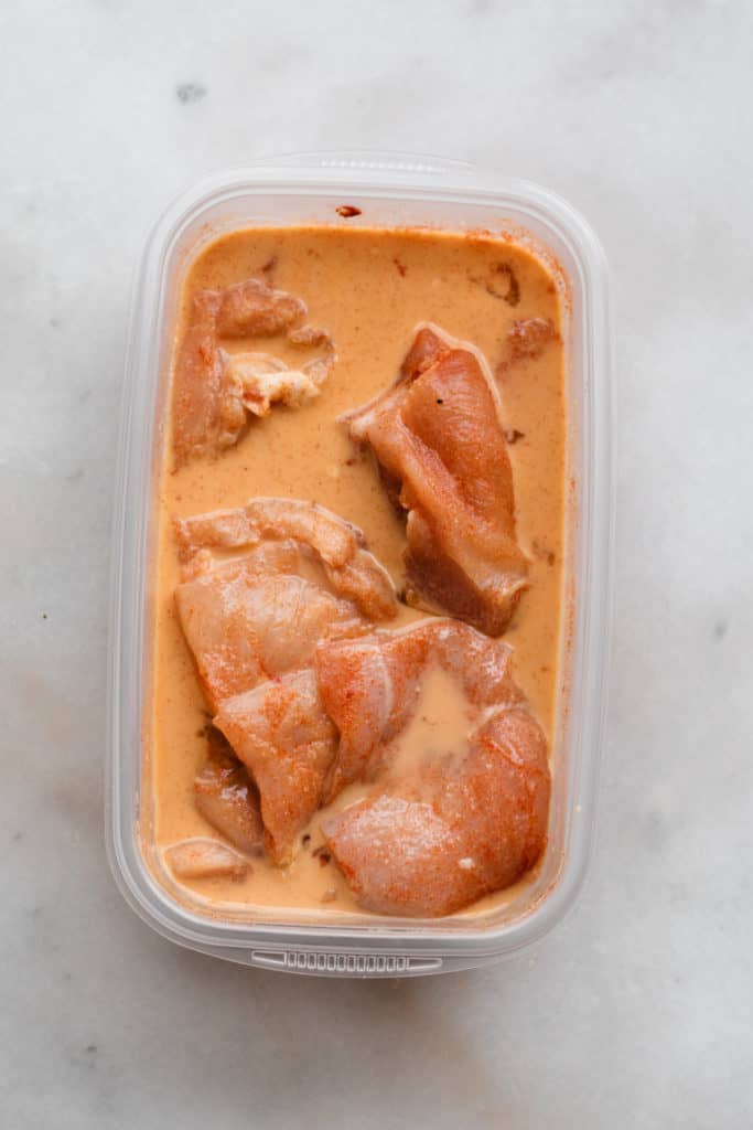Chicken pieces in a buttermilk, egg, and spice mixture on a marble surface