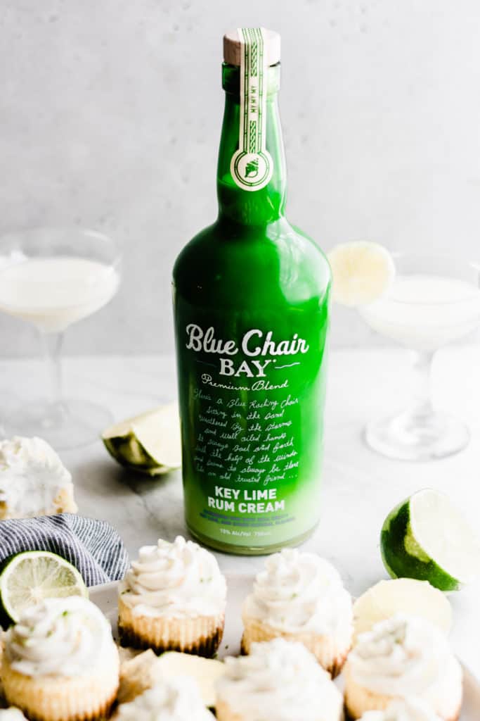 A bright green bottle of Blue Chair Bay Key Lime Rum Cream with two glasses of rum and a few lime slices in the background