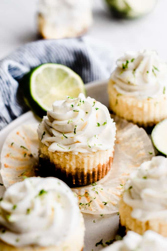 A plate of mini key lime cheesecakes topped with whipped cream and lime zest. 