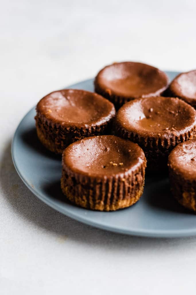 Mini chocolate cheesecakes sitting on a blue plate, on a gray surface