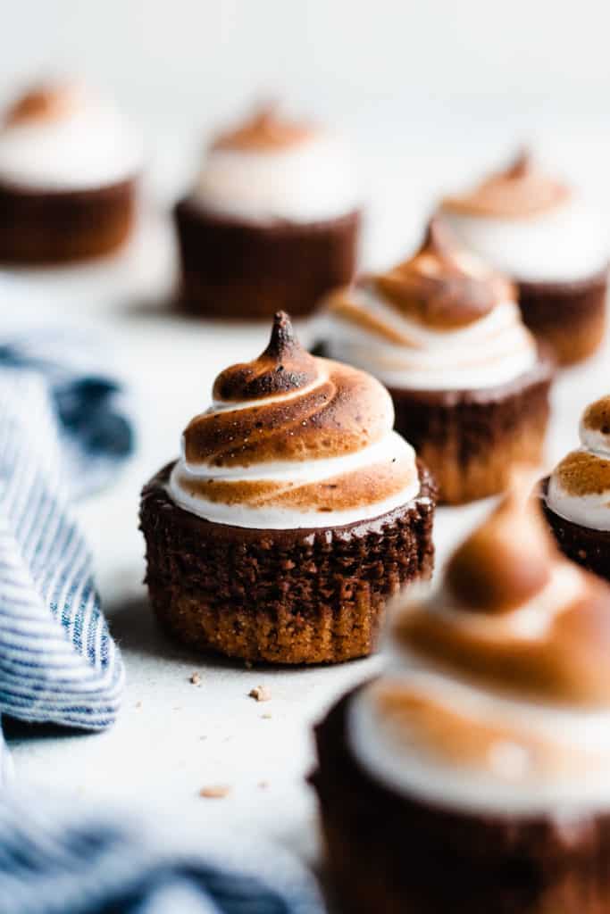 Mini S'mores Cheesecakes with Toasted Meringue on a gray surface, with a blue striped linen