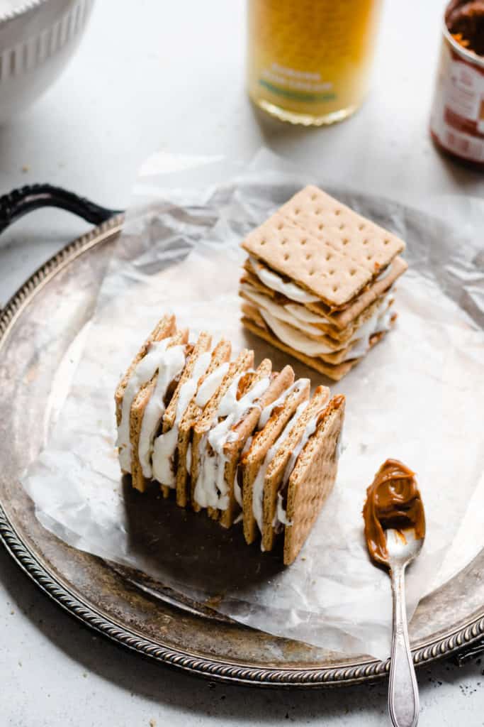 A stack of graham crackers sandwiched with whipped cream and dulce de leche on a lined platter