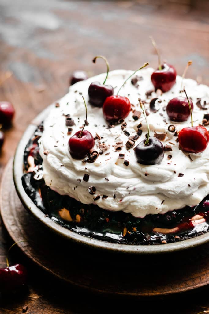 A Black Forest Pie, topped with a pile of whipped cream and fresh cherries, on a vintage wooden surface