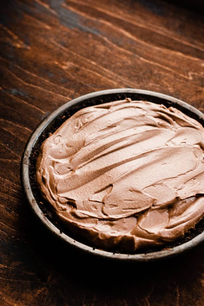 Chocolate mousse filling in a chocolate crust in a metal pie plate on a wooden surface