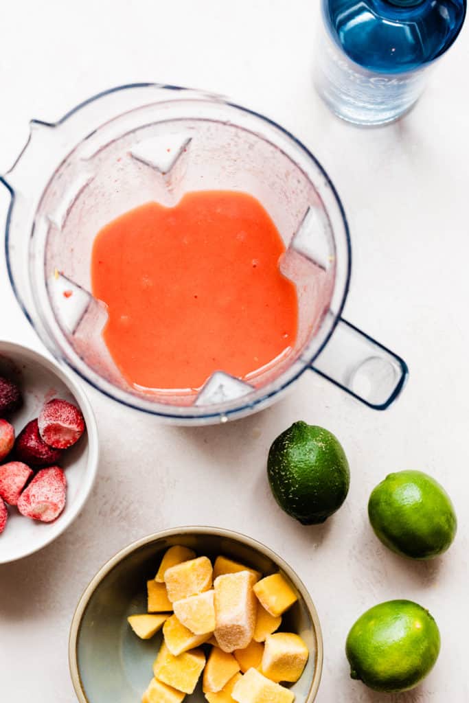 The pinky orange cocktail mixture blended up in the blender, with fruit scattered around