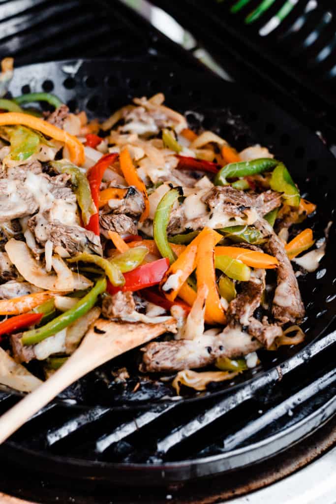 A wooden spoon rests in a grill pan filled with the cooked beef, pepper, onion, and cheese mixture