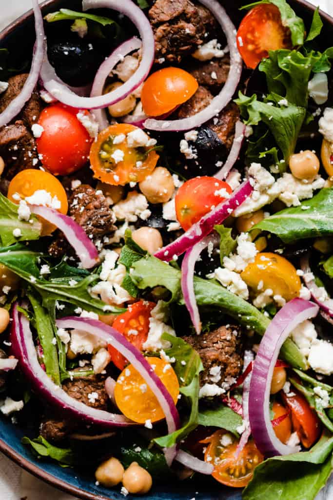 A close-up of the tossed salad with red onion, lettuce, cherry tomatoes, feta, black olives, and lamb