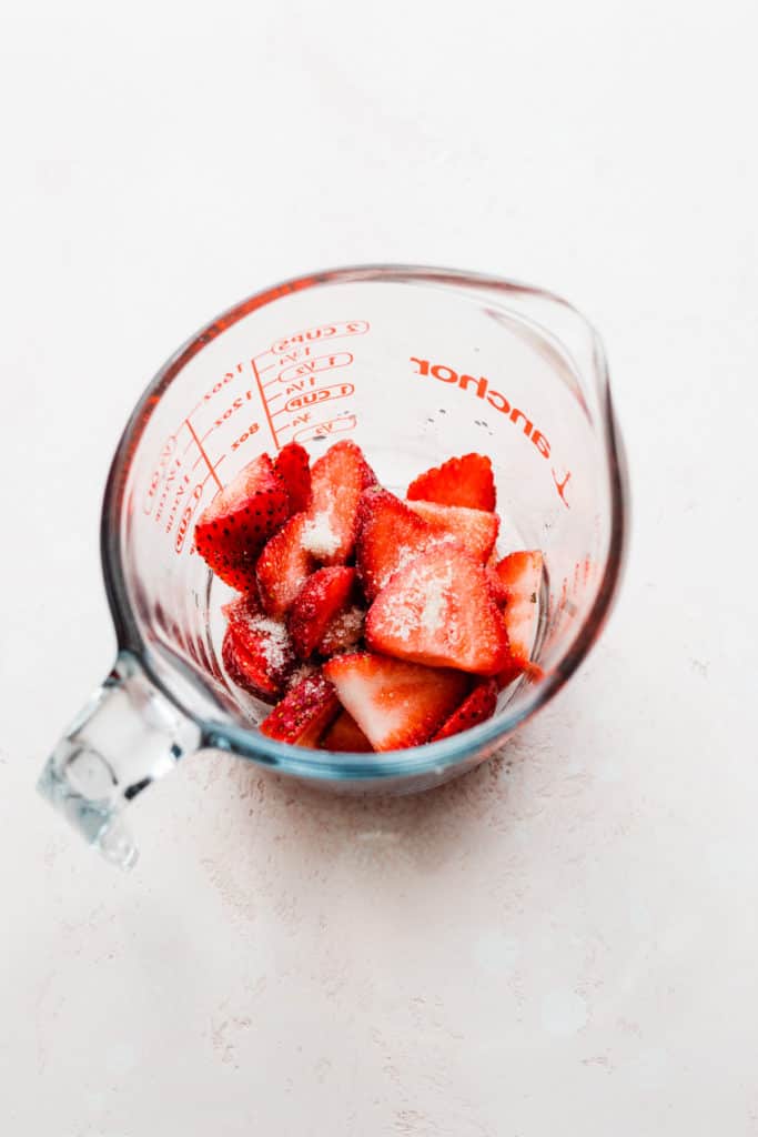 Sliced strawberries in a glass measuring cup with a sprinkle of sugar