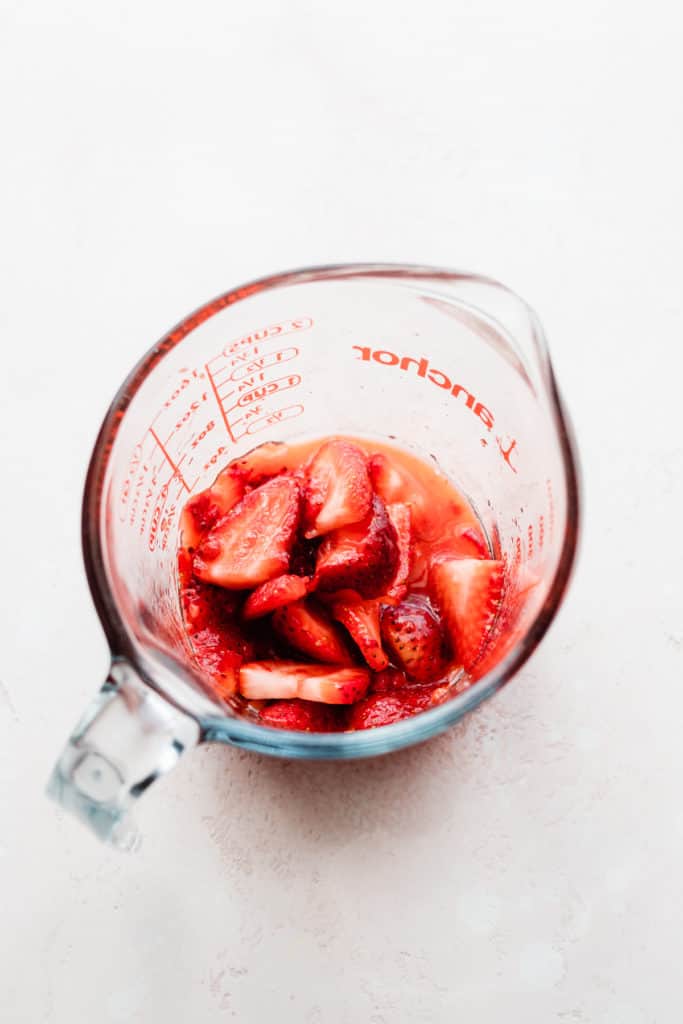 A glass measuring cup with juicy muddled strawberries 