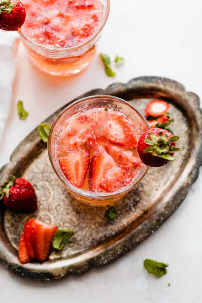 Two glasses of a pink cocktail with strawberries floating in the glass, on a vintage metal tray