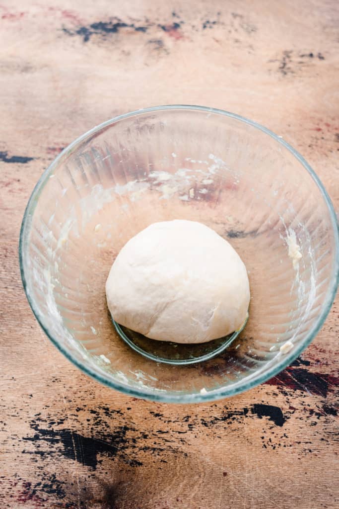 A glass bowl with unrisen pizza dough on a wooden surface