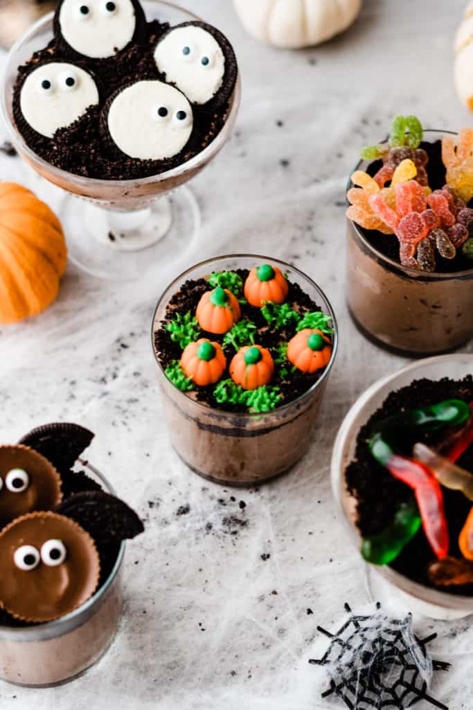 A dirt cup topped with green frosting grass and candy pumpkins