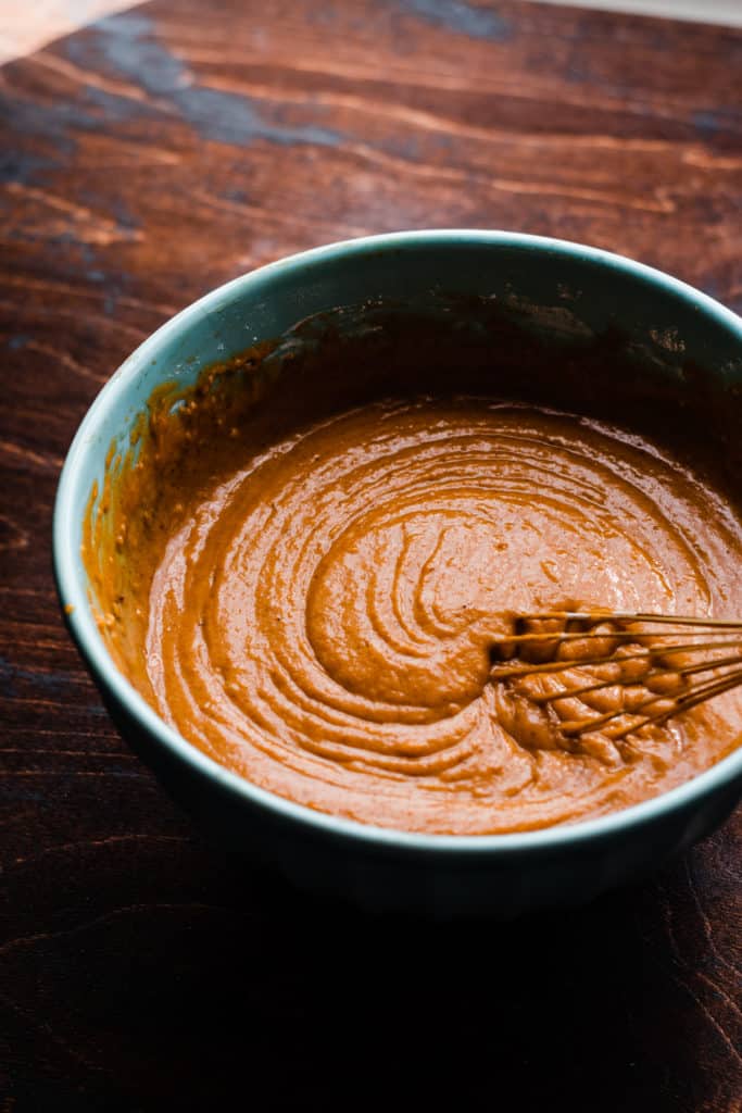 A bowl of creamy pumpkin cupcake batter being whisked, on a wooden surface