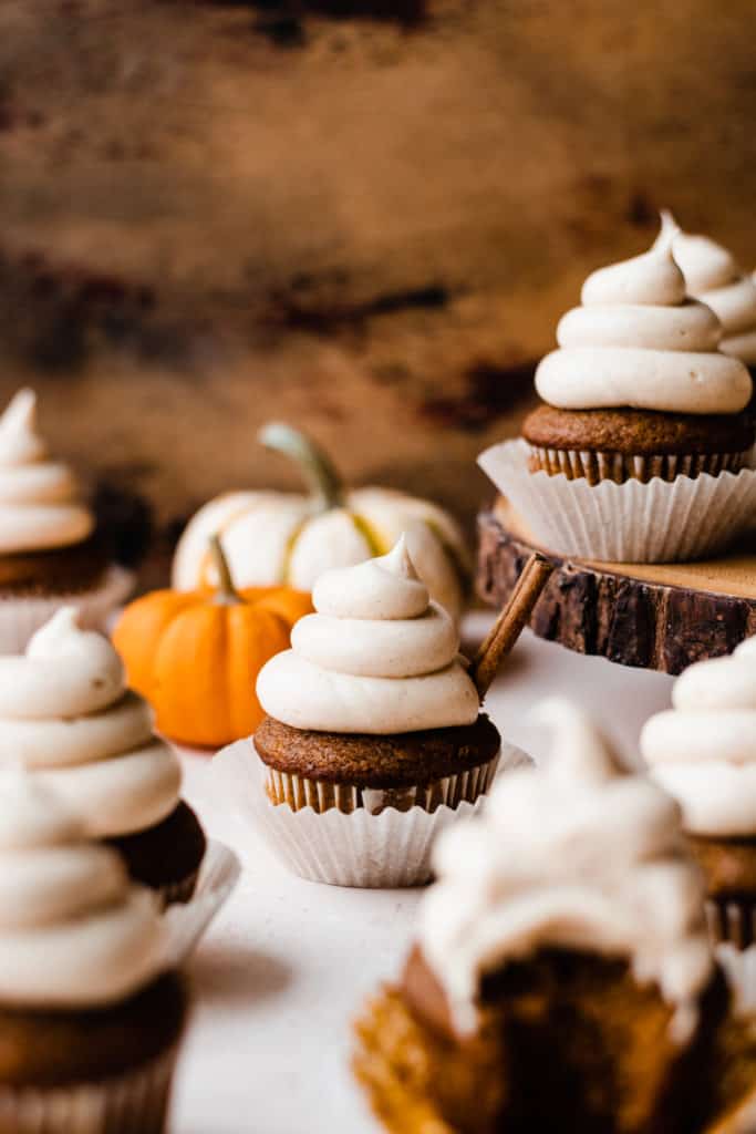 Straight-on shot of a few pumpkin cupcakes, with mini pumpkins in the background