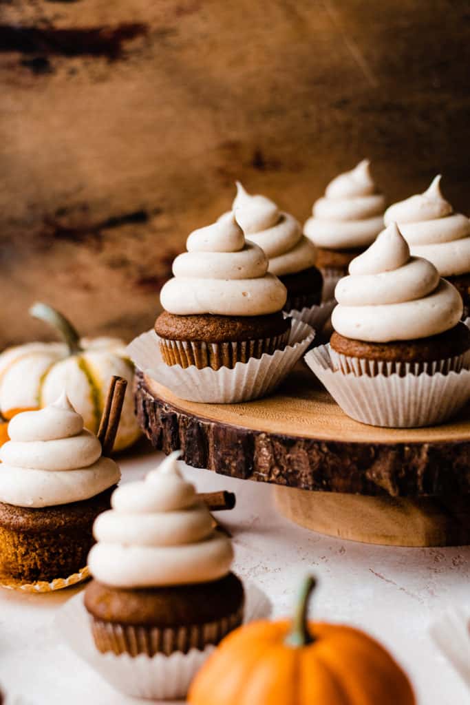 Frosted pumpkin cupcakes on a rustic wooden cake stand